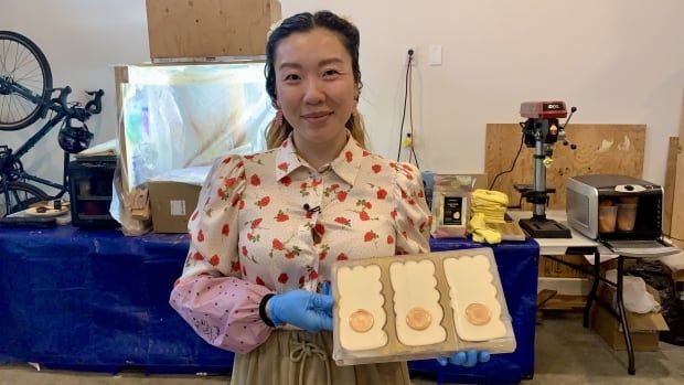 A woman holds a tray of molds filled with white chocolate.