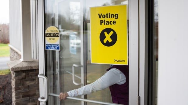 A yellow sign that says voting place is posted on a door as a hand opens it.