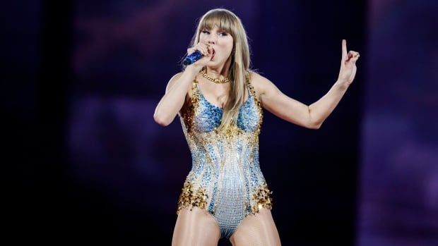 A blond-haired woman in a blue-tinged sequined dress sings into a microphone with her head tilted and her arm extended, a finger pointing up into the air.