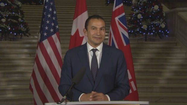 A man stands at the podium with a trio of flags behind him.