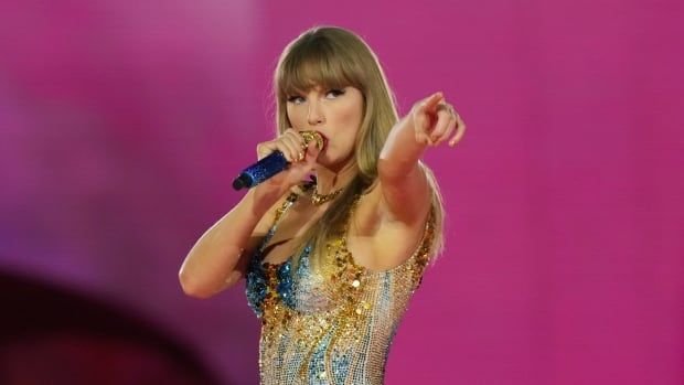 A woman with blond hair in a blue-tinged sequined dress sings into a blue and gold-tipped microphone while pointing at the Rogers Centre crowd.