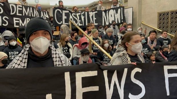 An image of Dozens of anti-war protestors shown occupying the lobby of the Confederation Building in Ottawa. 