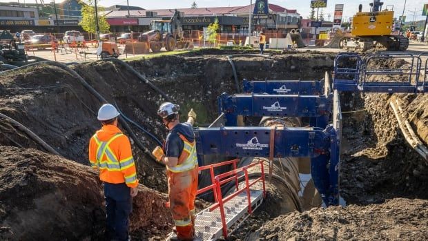 Two workmen stand next to an exposed section of water main pipe.