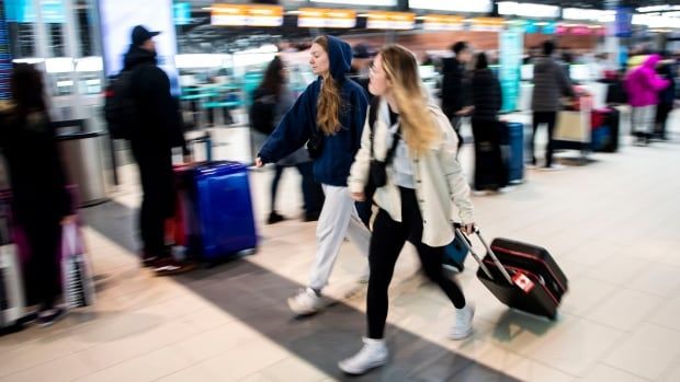 Two women walk by a line up of other travellers at an airport checkin terminal.