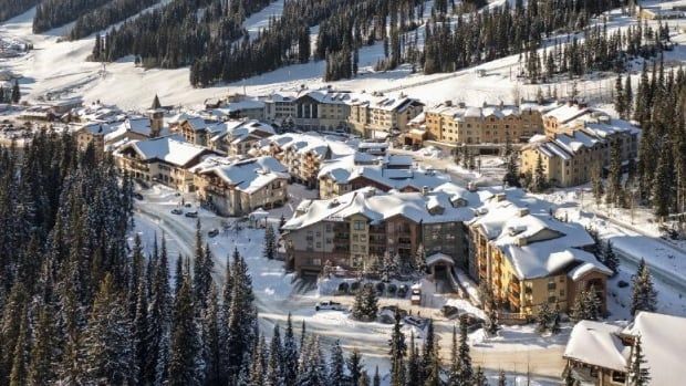 Snow covers the rooftops of a chalet-style community nestled in the middle of the mountains.