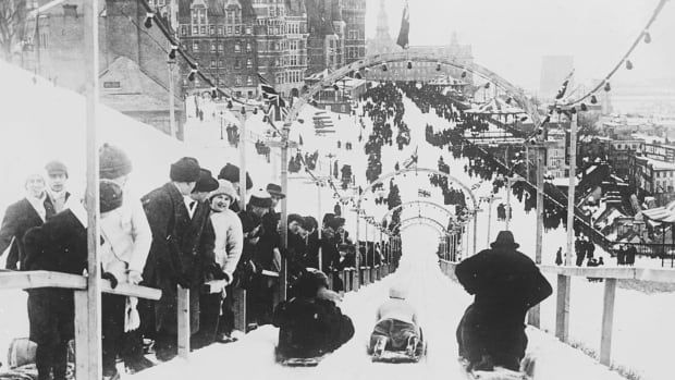 Old black and white picture of people sliding down a large slide in winter.