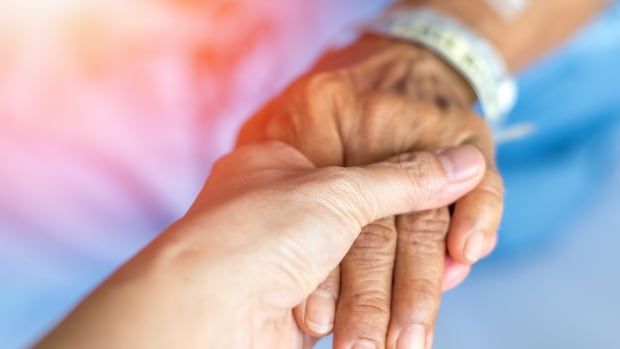 A doctor's hand on the hand of a senior patient in hospital examination room or hospice nursing home.