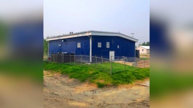 A large blue building is seen surrounded by green grass and brown mud.