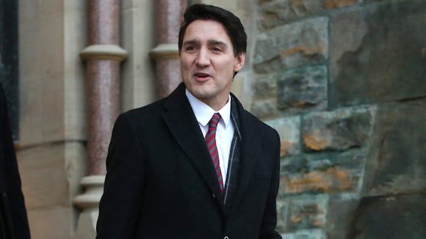 Man in suit smiles at camera while walking out of building.