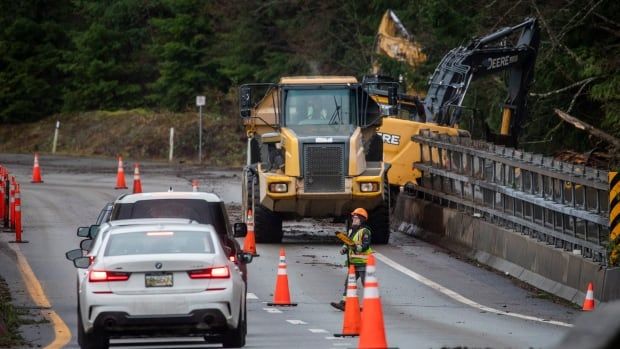 A worker wearing a high vis vest and a truck loader are pictured along the side of a highway.