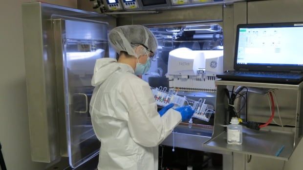 A picture of a person wearing glasses and a lab coat standing in front of an open door holding tubes in a medical laboratory. 