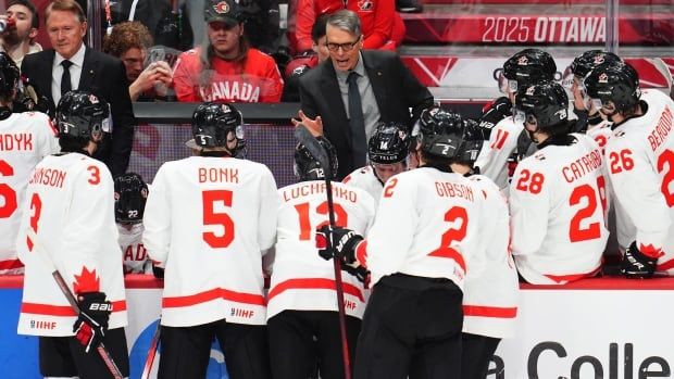 Male hockey coach speaks on the bench to team.