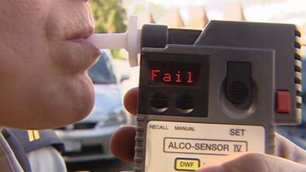 Person blowing into breathalyzer device with the reading "Fail" in red neon letters.