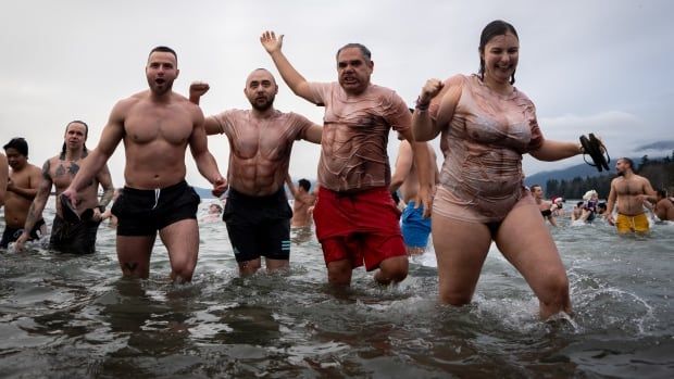 A group of people wearing thin shirts resembling bodybuilder costumes smile as they take part in a cold plunge.