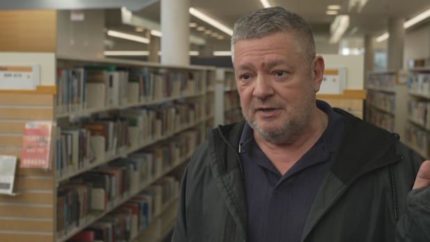 A man standing in the middle of an aisle of books in the library.