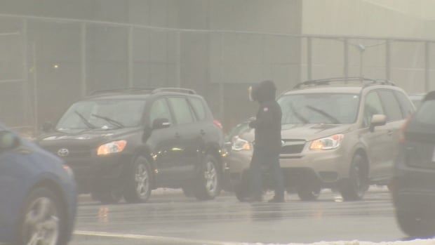 A pedestrian makes their way across a busy intersection, as snow and rain fall in St. John's.