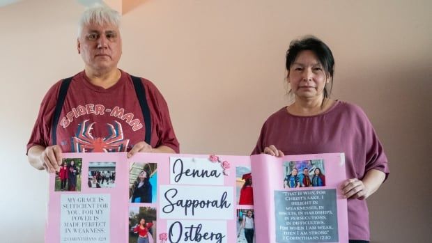 Two people stand in a room, holding a poster.