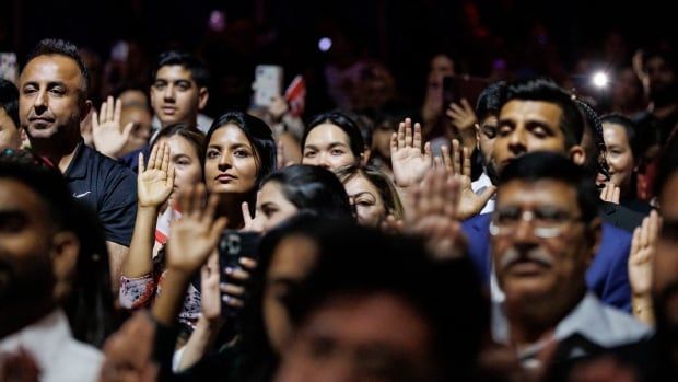 Soon-to-be citizens of Canada raise their hands during a citizenship ceremony.