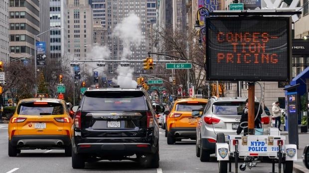 A sign that reads congestion pricing sits on the side of a busy Manhattan road.