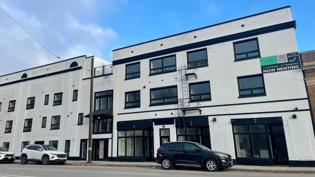 white and black building with a "now renting" sign hung up