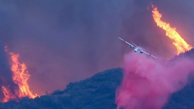 A firefighting aircraft drops fire retardant as the Palisades Fire burns near a hilltop amid a powerful windstorm 