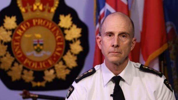 Man in white dress police shirt sits in front of an Ontario Provincial Police backdrop.