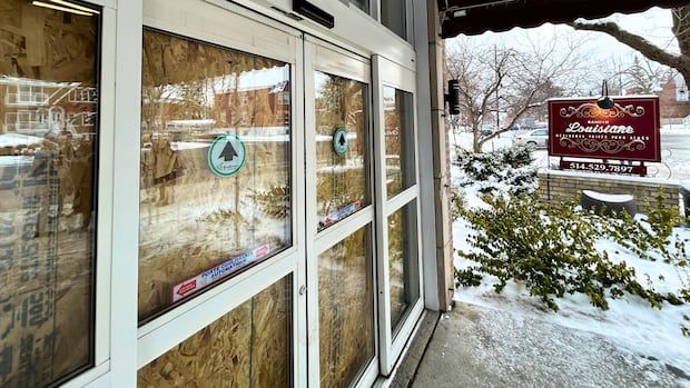 The front sliding doors of a building are boarded up on the inside with a sign in background reading Manoir Louisiane