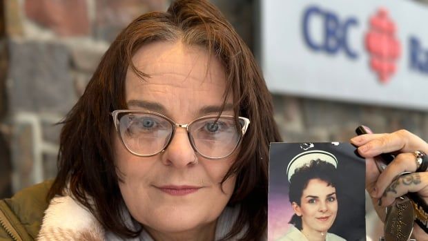 A woman holds up a photograph of her younger self wearing a nurse's uniform. 