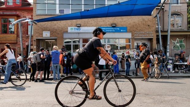 A woman bikes past a building where people are holding a rally. 