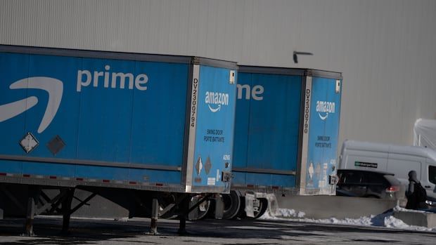 An employee walks past large blue trucks at Amazon's DXT4 warehouse in Laval, Que.