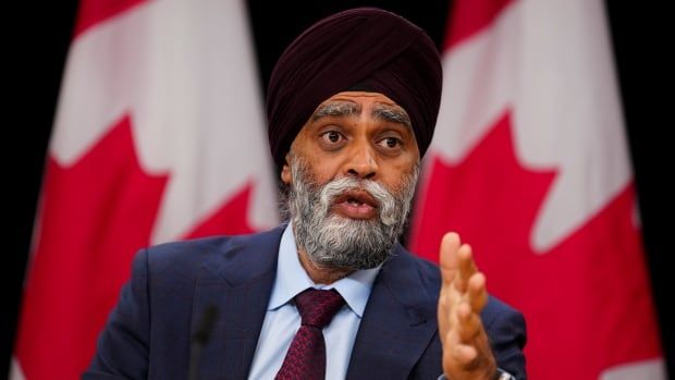 A South Asian man with a turban sits in front of Canadian flags.