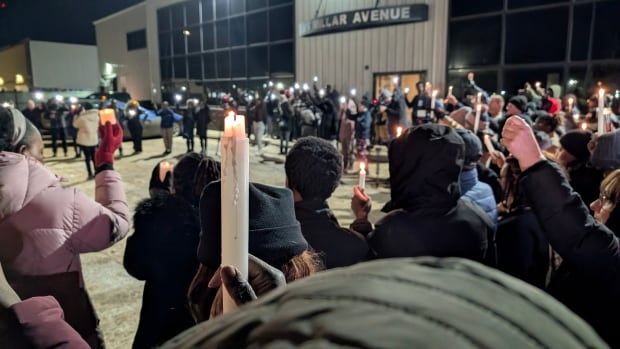 A wide shot of many people holding up candles in a snowy area at night.