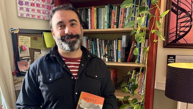 A man poses for the camera holding a book in front of a bookshelf