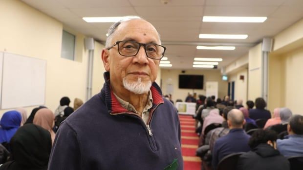 A man looks at the camera. Stanidn inside of a room with people sitting in chairs