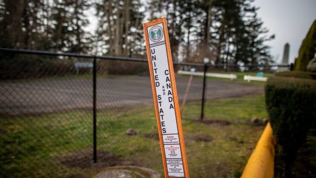 Canada/US sign in front of fence.