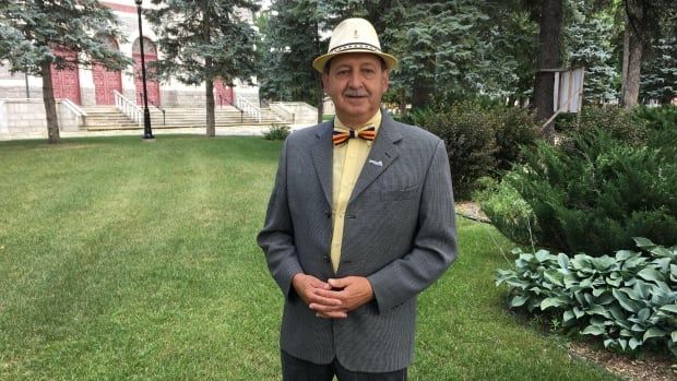 A man in a suit and wearing a hat and bow-tie smiles at the camera