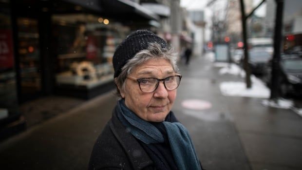 A person in a toque and blue scarf is seen on a street on a snowy day.