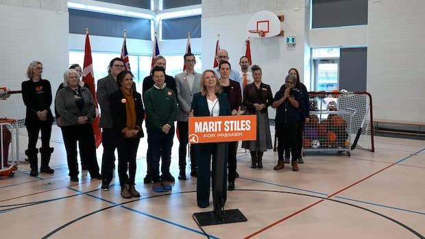 Marit Stiles stands at a podium in a gym surrounded by her campaign team.