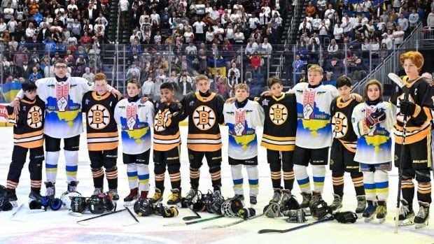 A group of young hockey players stand interlocking arms, on the ice before a hockey game.