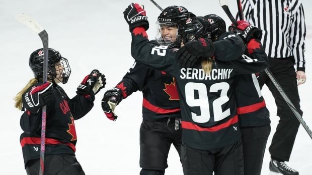 A group of female ice hockey players smile while wrapping their arms around each other in celebration during a game.