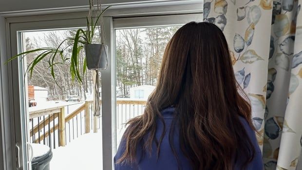 The back of a woman's head while she looks out the window. She has long brown hair. The ground is covered with snow. 