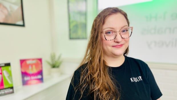  A portrait of Taylor Caldwell with glasses and a black t-shirt inside the cannabis shop she manages.