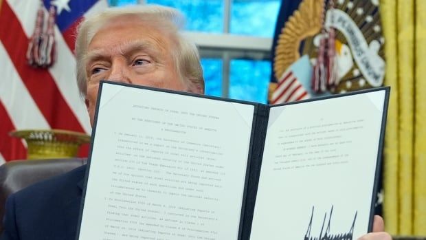 A man sits at a desk and holds up a folder.