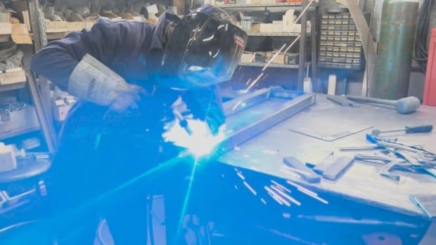 a person in a full head visor uses a welder on metal, with fire and sparks