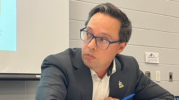 A man in a suit, but no tie, listens carefully during a public meeting. 