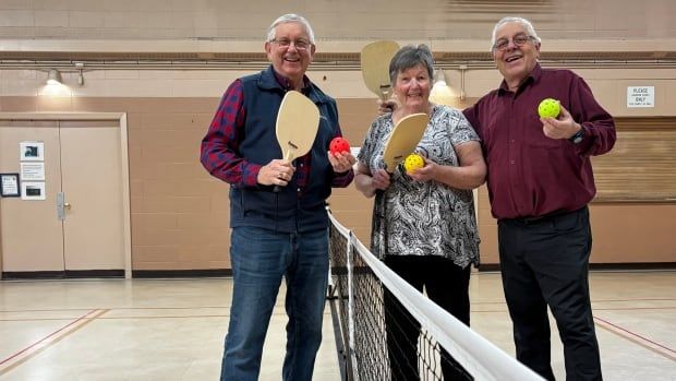 People stand behind a pickleball net holding paddles and balls. 