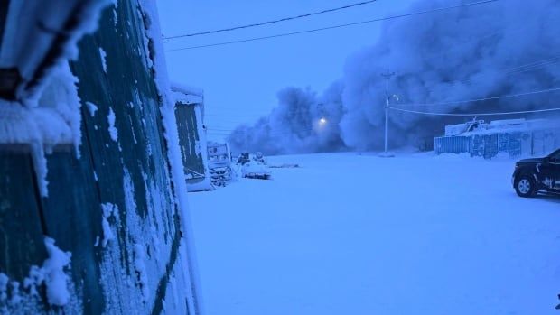 Smoke billows from a building down the street on a dark morning with lots of snow covering the buildings 