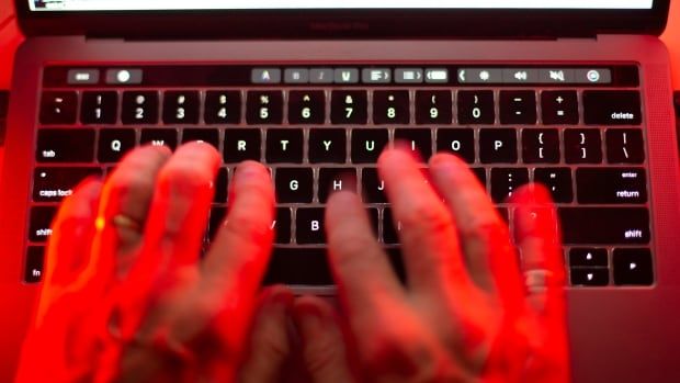 Two hands are typing on an Apple laptop keyboard, lit by a red light. 