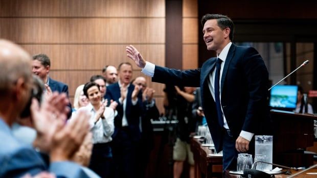 A man in a suit raises his hand as a crowd applauds him.