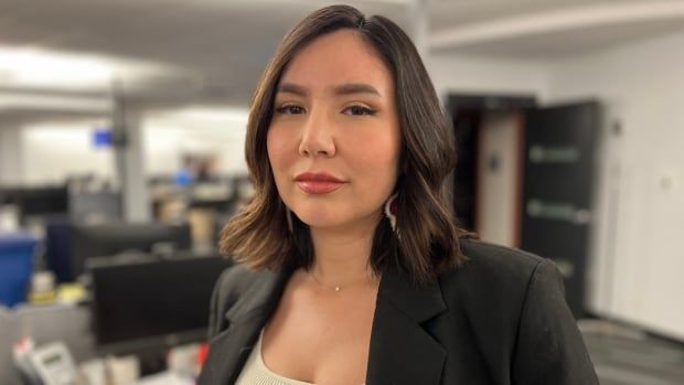 A woman with medium-length brown hair and wearing a black blazer looks into the camera.